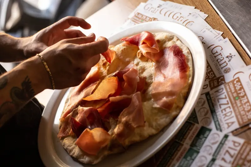 Mani che servono una pizza con prosciutto crudo