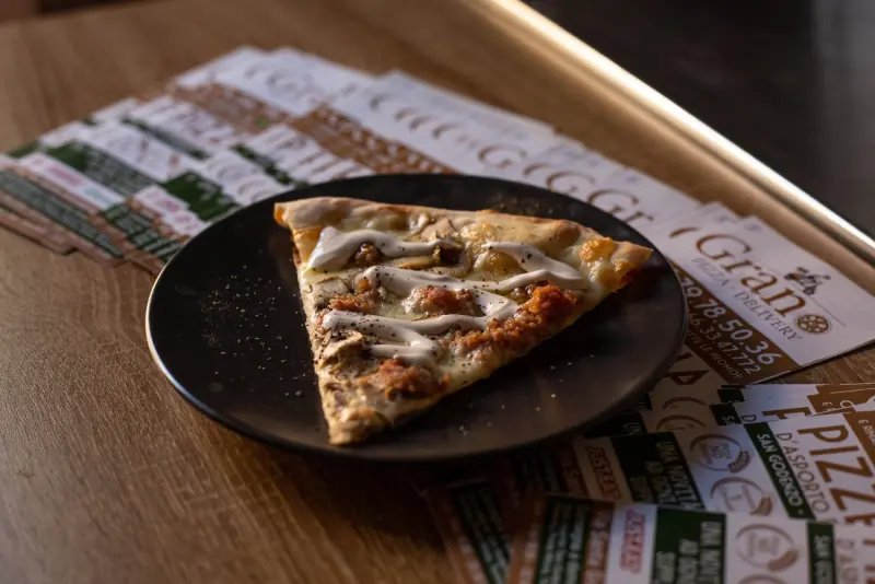 Uno spicchio di pizza bianca sul banco tra i volantini Grano